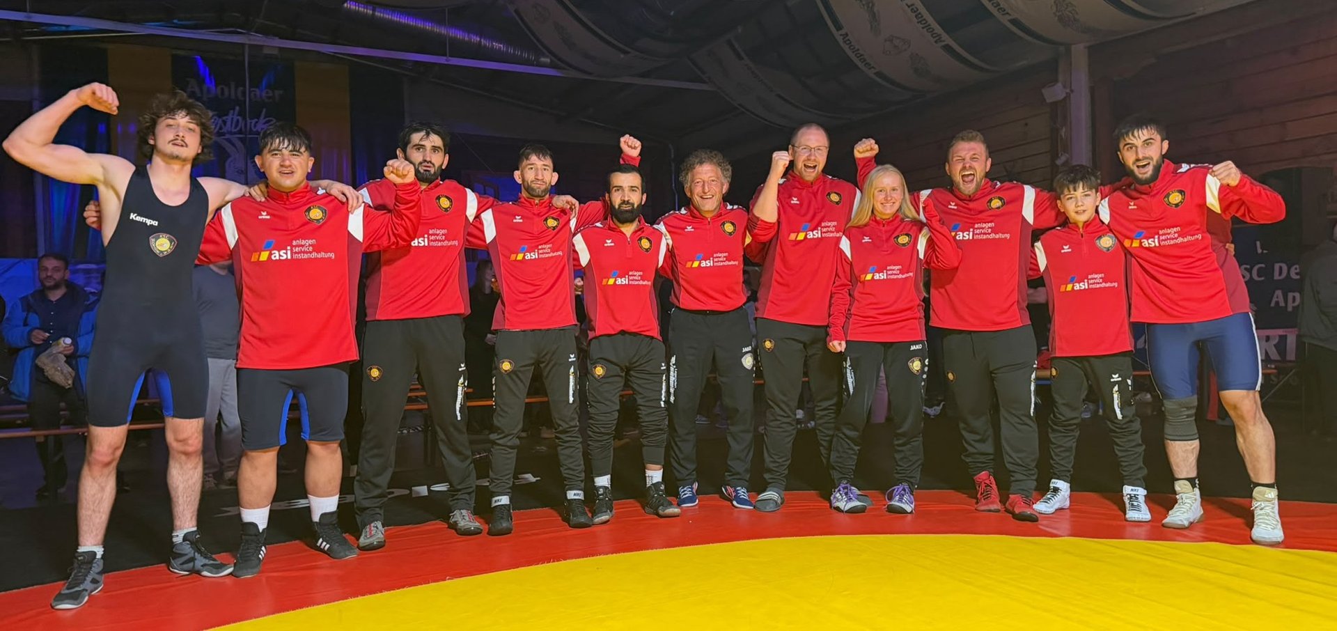 Ringerinnen, Ringer und Betreuer des KSC Motor Jena jubeln nach dem 19:13-Auswärtssieg auf der Matte in Apolda